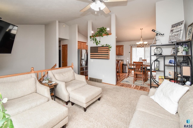 living room with visible vents, baseboards, ceiling fan with notable chandelier, vaulted ceiling, and light colored carpet