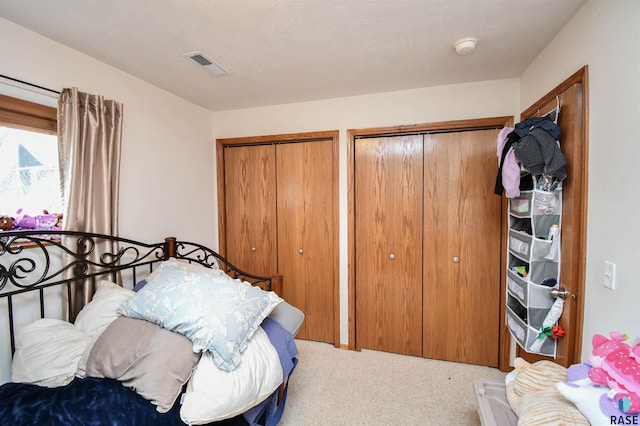 bedroom with visible vents, two closets, and carpet