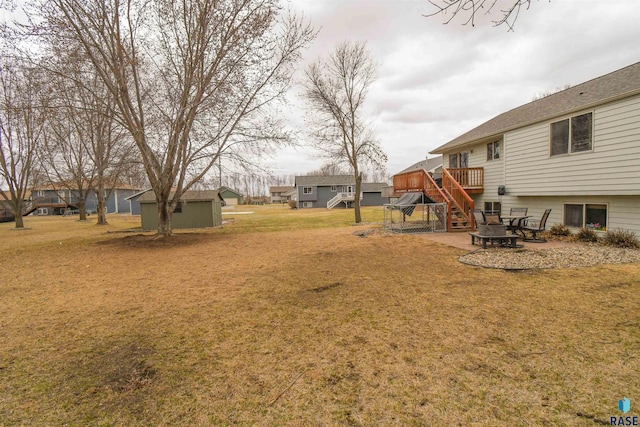 view of yard with stairway, an outdoor fire pit, a wooden deck, an outdoor structure, and a storage unit