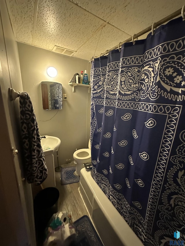 full bathroom with toilet, wood finished floors, shower / bath combo with shower curtain, visible vents, and a paneled ceiling