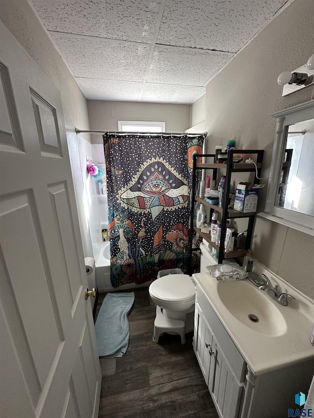 bathroom with toilet, vanity, wood finished floors, shower / bath combo with shower curtain, and a drop ceiling