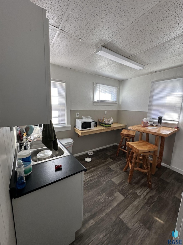 kitchen featuring a sink, a drop ceiling, white microwave, and dark wood-type flooring