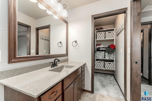 bathroom with a spacious closet, vanity, and baseboards