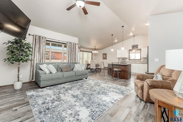 living area featuring ceiling fan with notable chandelier, lofted ceiling, baseboards, and light wood-type flooring
