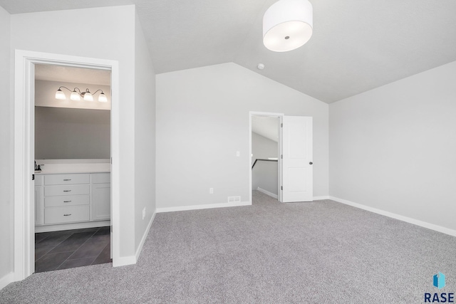 unfurnished bedroom featuring baseboards, lofted ceiling, a walk in closet, and carpet