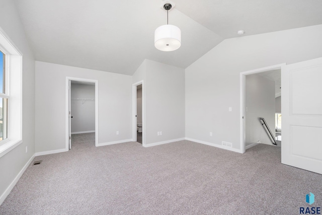 unfurnished bedroom with a walk in closet, light carpet, vaulted ceiling, and visible vents