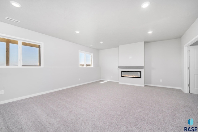 unfurnished living room featuring carpet flooring, recessed lighting, a glass covered fireplace, and visible vents