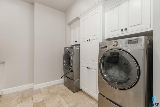 laundry area featuring baseboards, cabinet space, stone tile flooring, and washer and clothes dryer