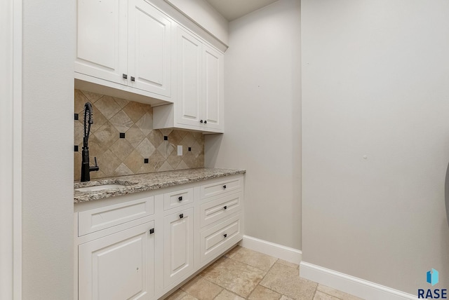 kitchen featuring white cabinets, baseboards, light stone countertops, backsplash, and stone tile floors
