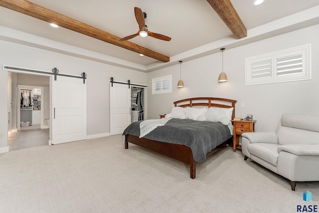 bedroom with a barn door, a walk in closet, beamed ceiling, and light colored carpet