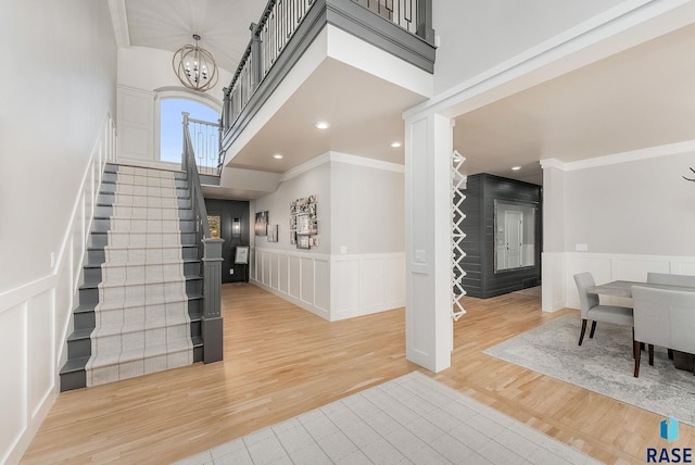 entrance foyer with crown molding, stairway, an inviting chandelier, a towering ceiling, and light wood finished floors