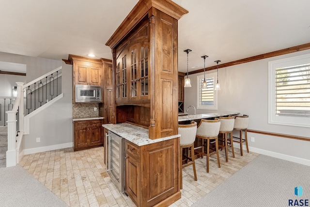 kitchen featuring stainless steel microwave, brown cabinets, beverage cooler, a breakfast bar area, and backsplash