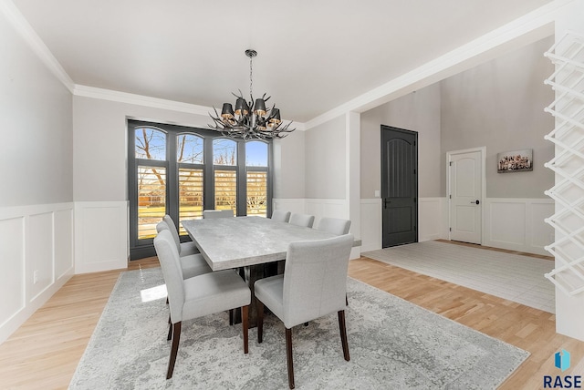 dining area with a wainscoted wall, light wood-type flooring, ornamental molding, and a chandelier