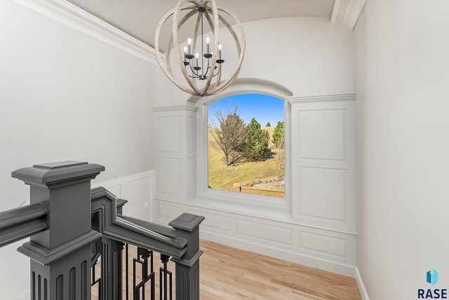 interior space with ornamental molding, a wainscoted wall, a decorative wall, a notable chandelier, and wood finished floors