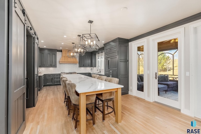 dining space with plenty of natural light, a notable chandelier, a barn door, and light wood-type flooring