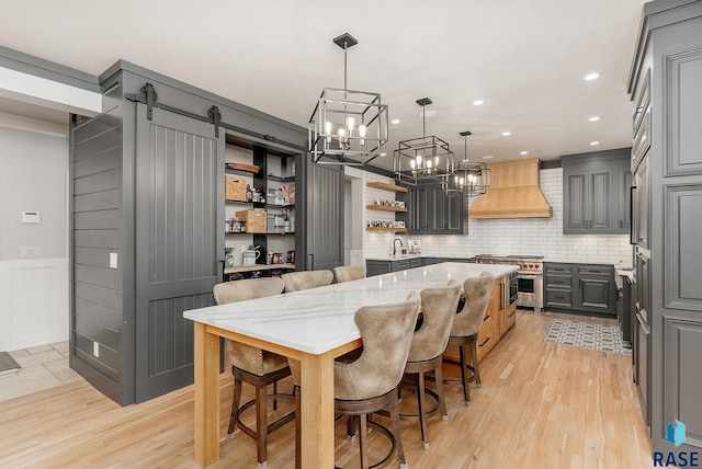 kitchen featuring light stone counters, high end stove, a kitchen bar, gray cabinetry, and custom exhaust hood