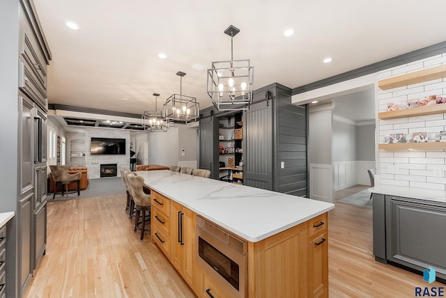 kitchen with open floor plan, open shelves, stainless steel microwave, a notable chandelier, and a fireplace