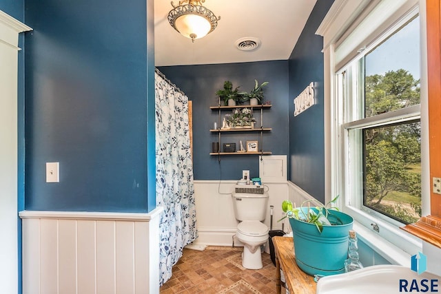 1220 NE 3rd St, Madison, SD 57042 - full bathroom featuring toilet, a sink, visible vents, curtained shower, and wainscoting