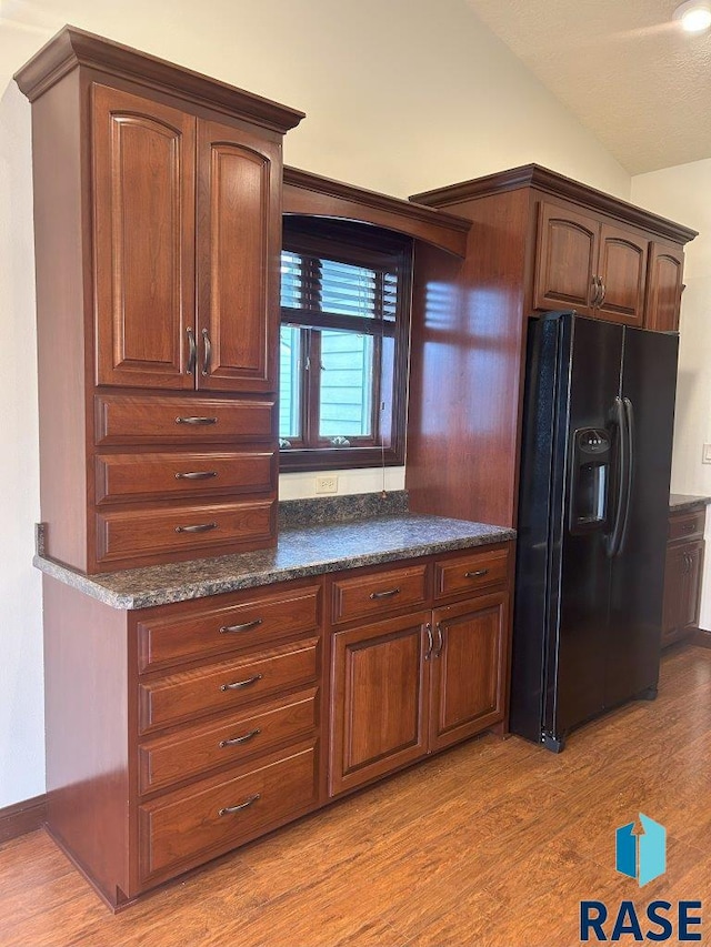 kitchen featuring black fridge with ice dispenser, dark countertops, light wood-style floors, and lofted ceiling