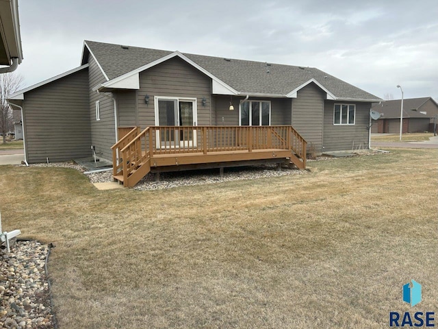 rear view of house with a wooden deck, roof with shingles, and a yard