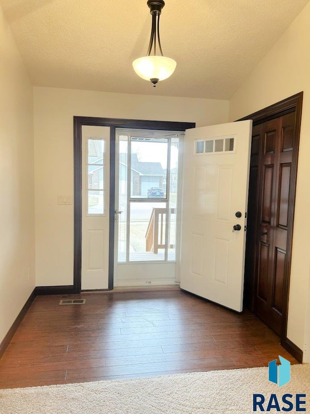 entryway featuring lofted ceiling, visible vents, wood finished floors, and a textured ceiling