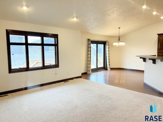 carpeted empty room with an inviting chandelier, visible vents, baseboards, and a textured ceiling