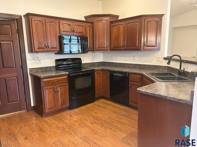 kitchen with a peninsula, wood finished floors, dark countertops, a sink, and black appliances