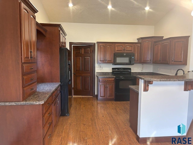 kitchen with dark wood-style flooring, black appliances, a breakfast bar, and a textured ceiling