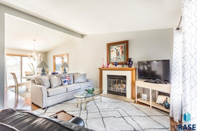 living room featuring lofted ceiling with beams, wood finished floors, a glass covered fireplace, and a notable chandelier