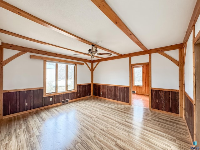 empty room with beam ceiling, wood finished floors, wainscoting, visible vents, and ceiling fan