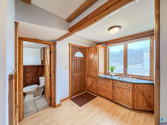 interior space with a wainscoted wall, toilet, beam ceiling, a sink, and wood finished floors