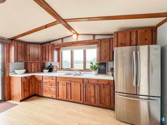 kitchen with light countertops, lofted ceiling with beams, a sink, freestanding refrigerator, and brown cabinetry