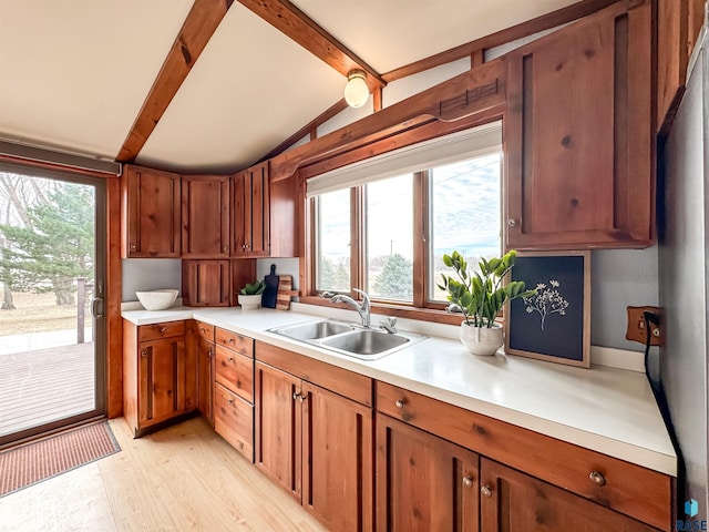 kitchen with light countertops, a sink, light wood-style flooring, vaulted ceiling with beams, and brown cabinets