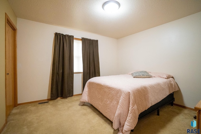 bedroom with a textured ceiling, baseboards, light colored carpet, and visible vents