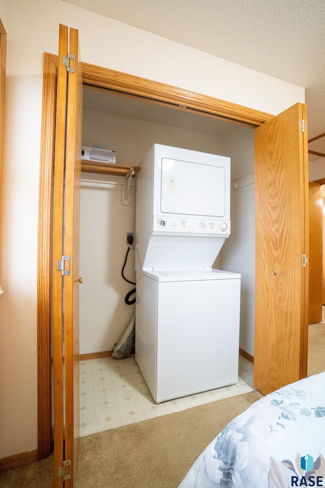 washroom with stacked washer and clothes dryer, baseboards, laundry area, and light floors