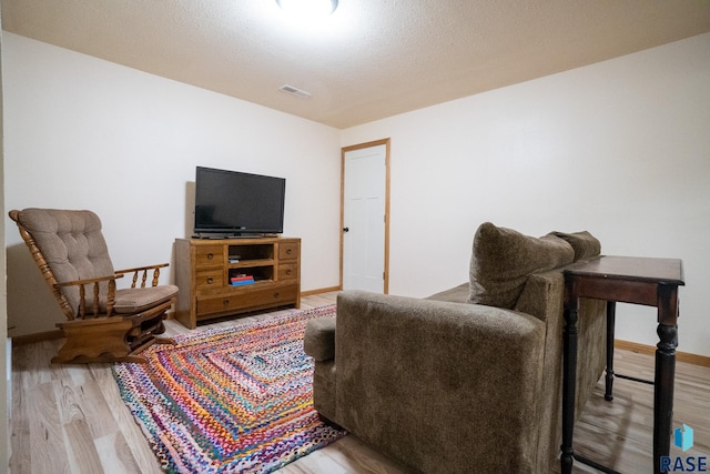 living room featuring wood finished floors, a textured ceiling, baseboards, and visible vents