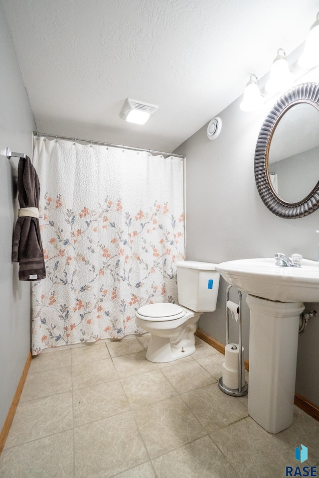 bathroom with toilet, visible vents, baseboards, and a textured ceiling
