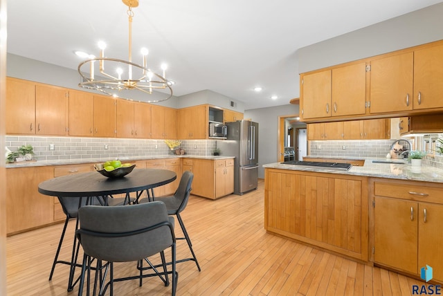 kitchen with a chandelier, a peninsula, stainless steel appliances, a sink, and light wood-type flooring