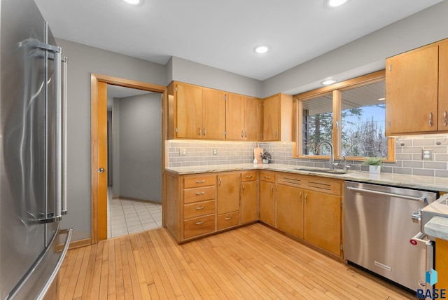kitchen with decorative backsplash, light wood-style flooring, appliances with stainless steel finishes, a sink, and light stone counters