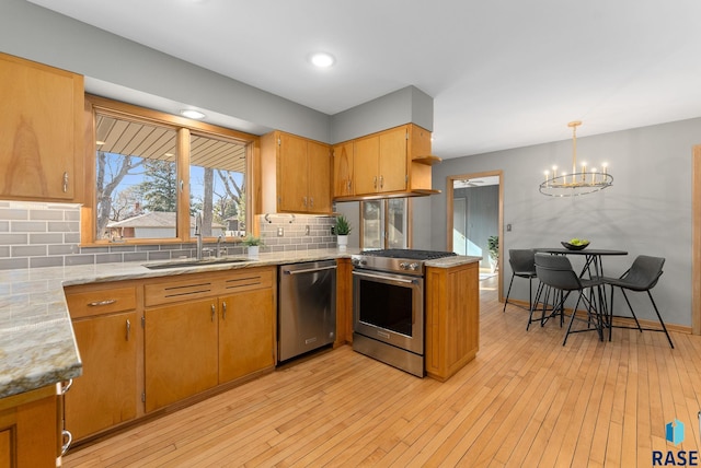 kitchen with a notable chandelier, a sink, tasteful backsplash, appliances with stainless steel finishes, and light wood-style flooring