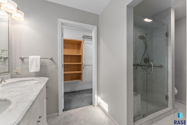 bathroom featuring a shower stall, baseboards, marble finish floor, a sink, and a walk in closet