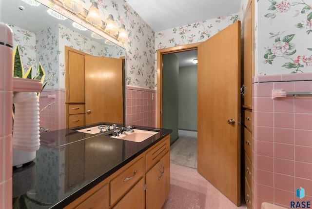 bathroom with a wainscoted wall, vanity, tile patterned flooring, wallpapered walls, and tile walls