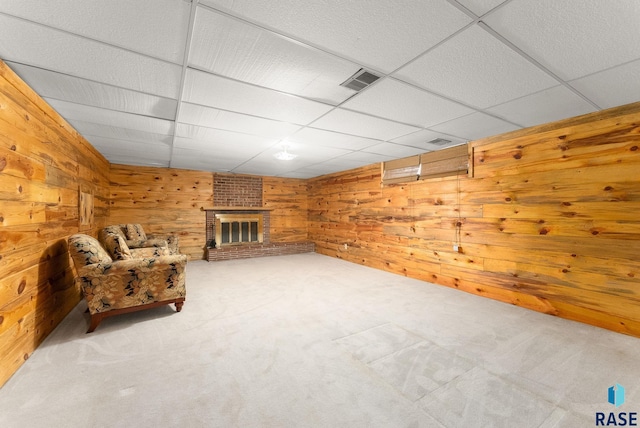 unfurnished room featuring visible vents, wooden walls, carpet, a fireplace, and a paneled ceiling