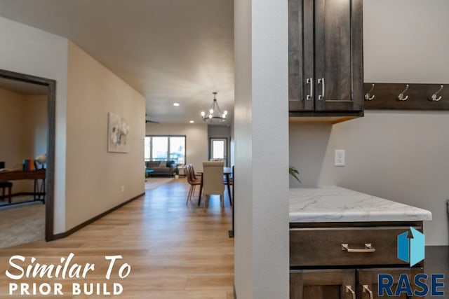 kitchen featuring a notable chandelier, light stone counters, baseboards, light wood-style floors, and dark brown cabinets
