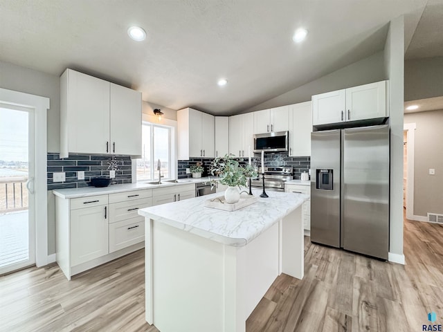 kitchen featuring a kitchen island, appliances with stainless steel finishes, a sink, light wood-style floors, and vaulted ceiling