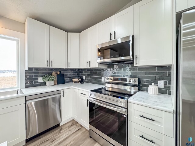 kitchen with white cabinetry, tasteful backsplash, stainless steel appliances, light wood-style floors, and light stone counters