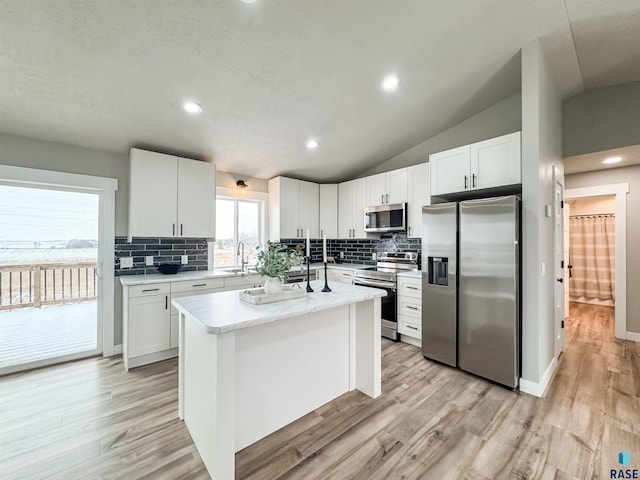 kitchen featuring lofted ceiling, stainless steel appliances, a sink, light wood finished floors, and white cabinets