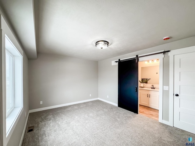 unfurnished bedroom with visible vents, baseboards, light carpet, a barn door, and a sink