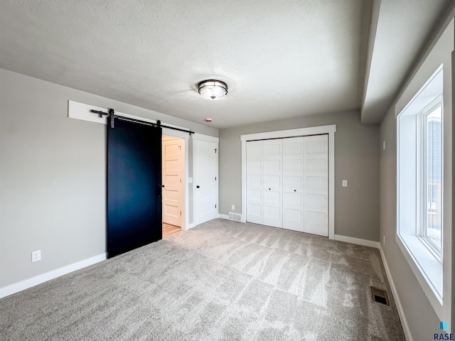 unfurnished bedroom featuring a closet, carpet flooring, visible vents, baseboards, and a barn door