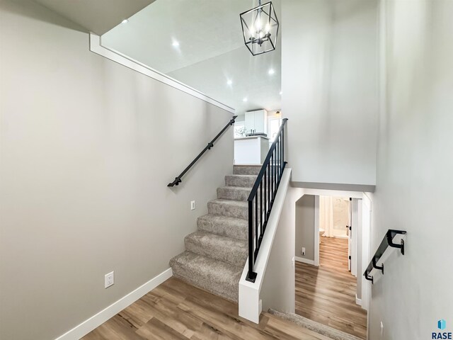 stairway with baseboards, a notable chandelier, and wood finished floors